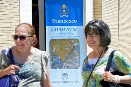 Turistas no Vaticano passam por cartaz sobre a encíclica papal que tratou do clima  Turistas no Vaticano